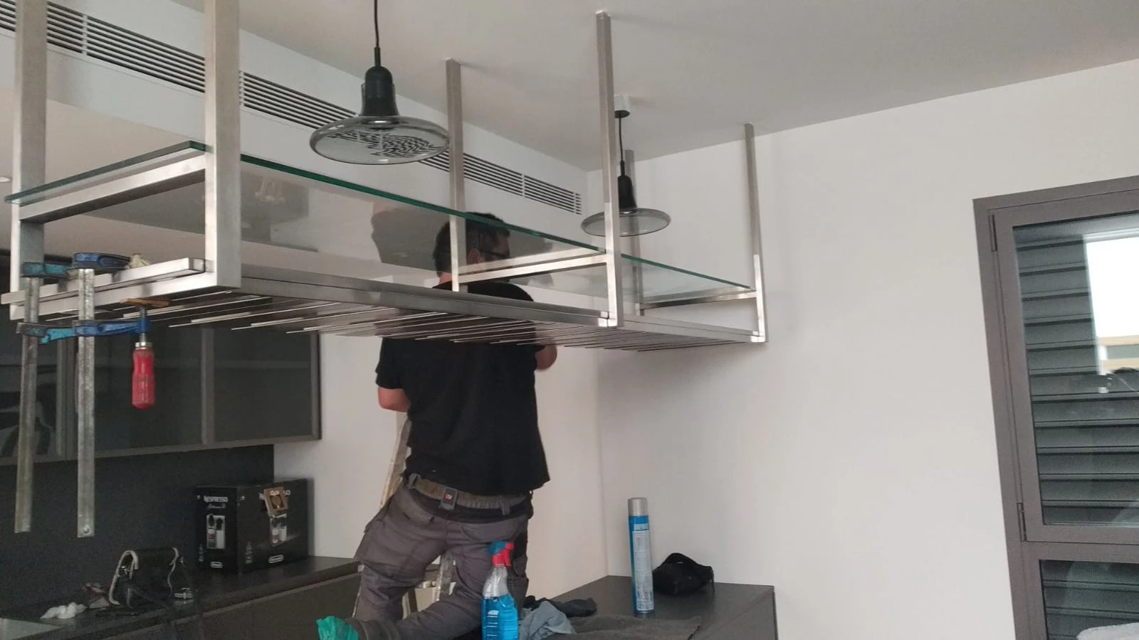 Operario instalando una estantería suspendida de acero inoxidable sobre una cocina